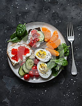 Breakfast, snack, tapas plate - sandwiches with red caviar, salmon, cream cheese, vegetables, spinach, boiled egg on a dark