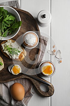 Breakfast with soft boiled eggs served on white wooden table, flat lay