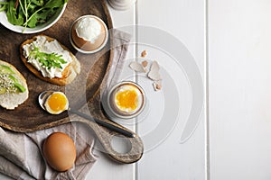 Breakfast with soft boiled eggs served on white wooden table, flat lay. Space for text