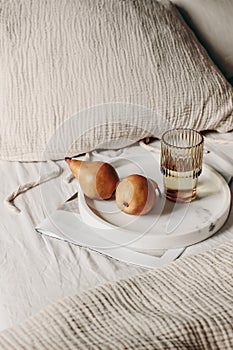 Breakfast still life composition. Glass of water, newspapers and pear fruit on white marble tray. White linen background