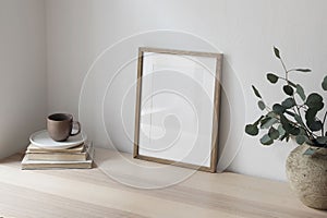 Breakfast still life. Cup of coffee, books. Empty wooden picture frame mockup on desk, table. Textured vase with silver