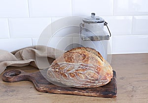 Breakfast still life. Fresh baked surdough bread on wooden chopping board. Kitchen interior. White tiled background