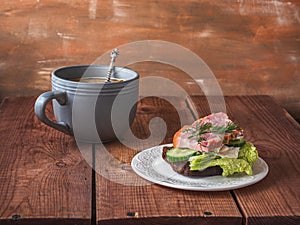 Breakfast with strong coffee in a large gray mug and ham and vegetables sandwich on a white plate