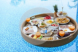 Breakfast in swimming pool, floating breakfast in tropical resort. Table relaxing in calm pool water, healthy breakfast and fruit