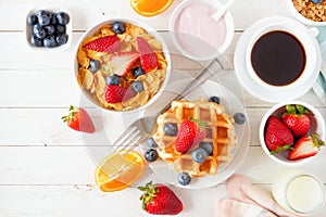Breakfast table scene with fruits, cereal, waffles, yogurt, milk and coffee. Top view over white wood.