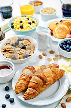 Breakfast table setting with flakes, juice, croissants, pancakes