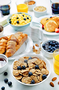 Breakfast table setting with flakes, juice, croissants, pancakes