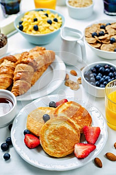 Breakfast table setting with flakes, juice, croissants, pancakes