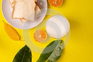 Breakfast table with sliced bread and glass of milk on yellow background