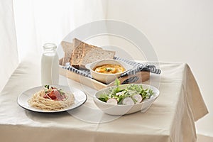 Breakfast table; spaghetti served with radish and salad with pumpkin puree, bread, milk set on table