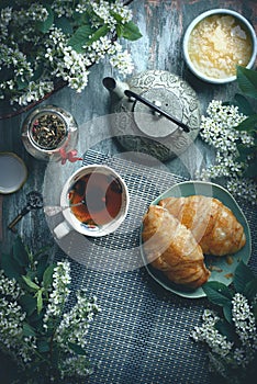Breakfast on table with tea, croissants and flowers, with copy space