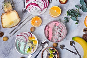 Breakfast table with yogurt acai bowls and fresh tropic fruits on a gray stone background with eucalyptus leaves, flat