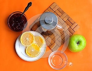 Breakfast tea in French press  lemon  cup  jam  apple  orange background  top view