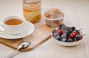 breakfast: tea with fresh berries, cake and honey/healthy breakfast: tea with fresh berries, cake and honey on a wooden surface.