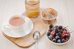 Breakfast: tea with fresh berries, cake and honey/healthy breakfast: tea with fresh berries, cake and honey on a wooden surface.