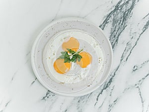 Breakfast is three eggs fried on a white plate on a white marble background.