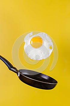 Breakfast time. A fried egg and a frying pan levitate in the air on a yellow background.