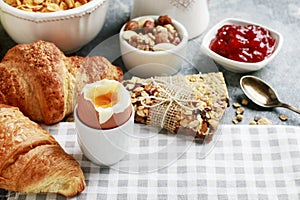 Breakfast time: soft-boiled egg, french croissants, muesli bars, milk