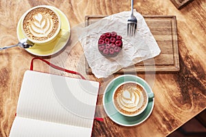 Breakfast time with two cups of fresh coffee from above on wooden background, sweet strawberry cake on wood board, opened book