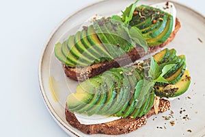 Breakfast toast with cream cheese and avocado on white plate, white background. Healthy food concept