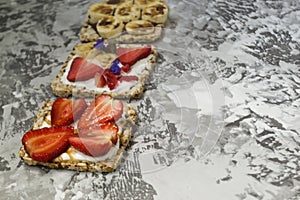 Breakfast with toaster and oat bread, buttered with butter, jam, strawberries and bananas on a concrete table.