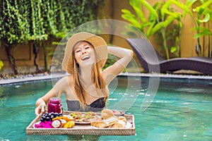 Breakfast tray in swimming pool, floating breakfast in luxury hotel. Girl relaxing in the pool drinking smoothies and