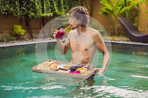 Breakfast tray in swimming pool, floating breakfast in luxury hotel. Man relaxing in the pool drinking smoothies and