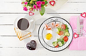 Breakfast on Valentine`s Day - fried egg in the shape of a heart, toasts, sausage and fresh vegetables.