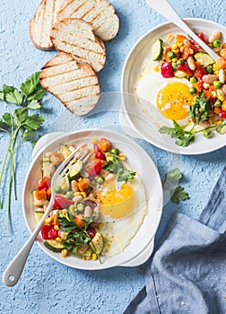 Breakfast vegetable hash with fried eggs on a blue background, top view. Healthy food