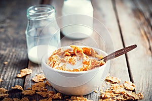 Breakfast wheat flakes in bowl and milk bottles on wooden