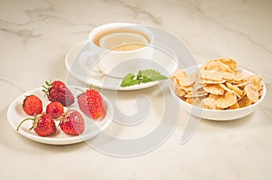 Breakfast on a white table/breakfast with strawberry, flakes, honey and tea with mint on a white background