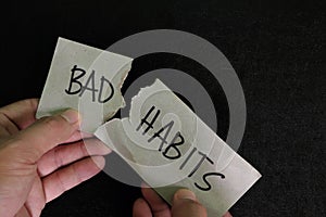 Breaking bad habits concept. Human hand tear a paper with word bad habit in dark black background.