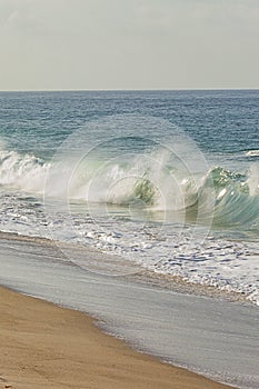 Breaking crashing wave on sandy shoreline with bloulders and iceplant