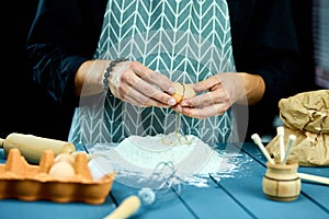 Breaking eggs in the flour. Close up of male hands breaking raw egg over flour. Baker kneading dough for cake.