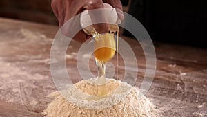 Breaking an fresh egg to a bunch of flour. Dough preparing process