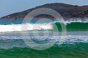 Breaking ocean wave with forested hill in the background.