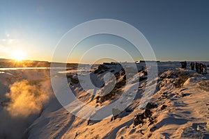 The breaking of the tectonic plates of the Gulfoss waterfall illuminated by the first rays of the dawn sun. Tourists watching and