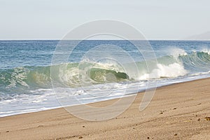 Breaking tube wave on sandy beach with foamy backwash, open expanse of ocean