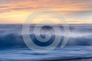 Breaking waves with spray at sunset over the sea