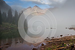 Breaks in the clouds express the early morning light on the Maroon Bells with a reflection of the peaks on Maroon Lake.