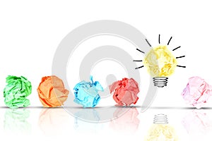 Breakthrough concept with multiple colorful crumpled pieces of paper around a yellow bright light bulb shaped paper on white backg