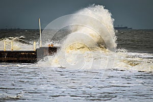 Breakwater and harbour in stormy weather with huge waves crashing over the walls pier. Abnormally strong storms in the middle