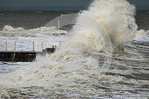 Breakwater and harbour in stormy weather with huge waves crashing over the walls pier. Abnormally strong storms in the middle