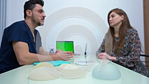 Breast augmentation implants indoors with blurred confident doctor talking to patient consulting woman. Side view of