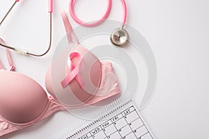 Breast cancer awareness concept. Top view photo of pink brassiere with pink ribbon stethoscope and calendar on isolated white