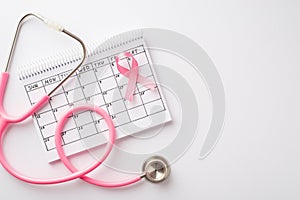 Breast cancer awareness concept. Top view photo of pink ribbon stethoscope and calendar on isolated white background