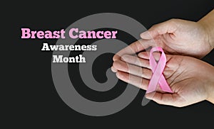 Breast Cancer Awareness Month. Woman hands holding pink ribbon on black background. International symbol of Breast