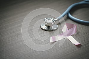 Breast cancer awareness pink ribbon with doctor stethoscope on wooden background, october symbol, healthcare and medicine concept