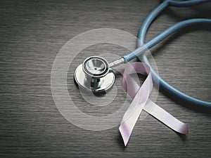 Breast cancer awareness pink ribbon with doctor stethoscope on wooden background, october symbol, healthcare and medicine concept