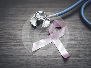 Breast cancer awareness pink ribbon with doctor stethoscope on wooden background, october symbol, healthcare and medicine concept